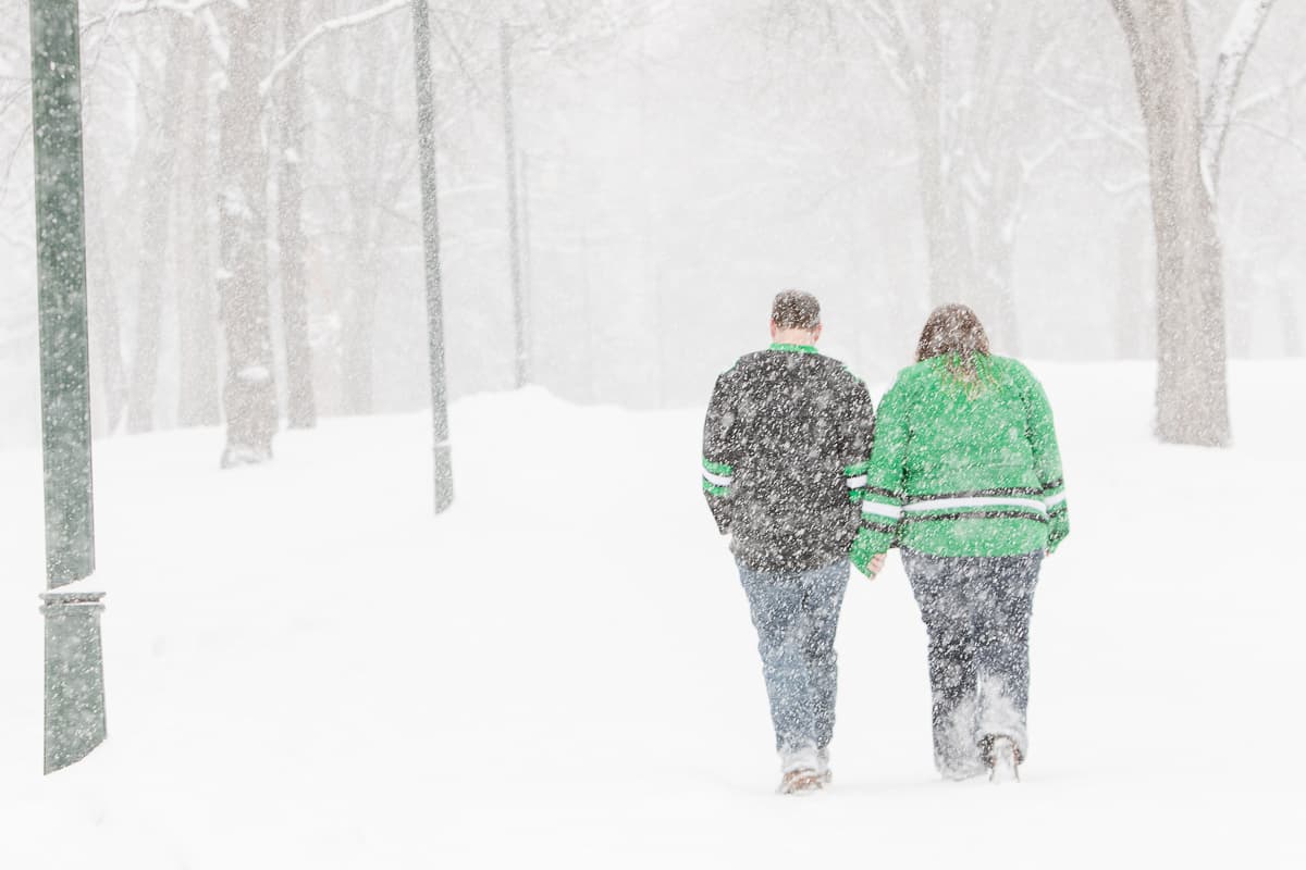 Amy and Dustin holding hands, walking away through heavy falling snow in a park.