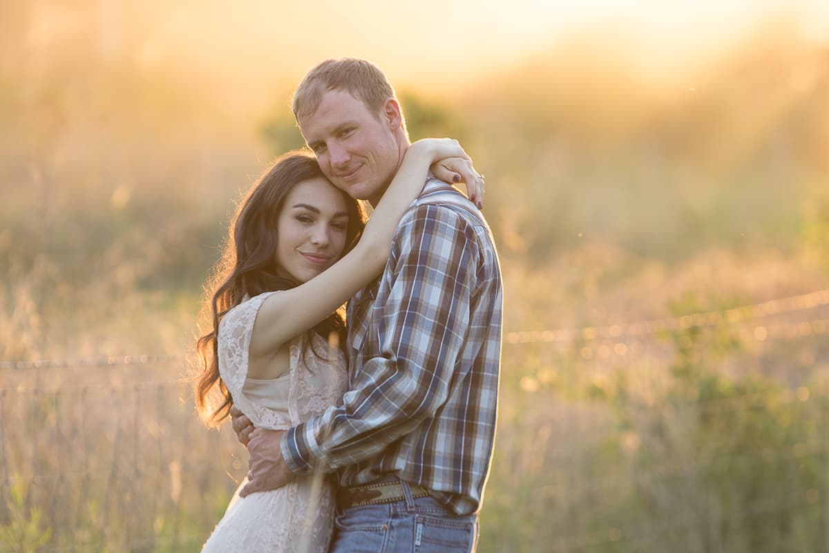 Sarah resting her head on August's shoulder in a field of tall grass at golden hour.