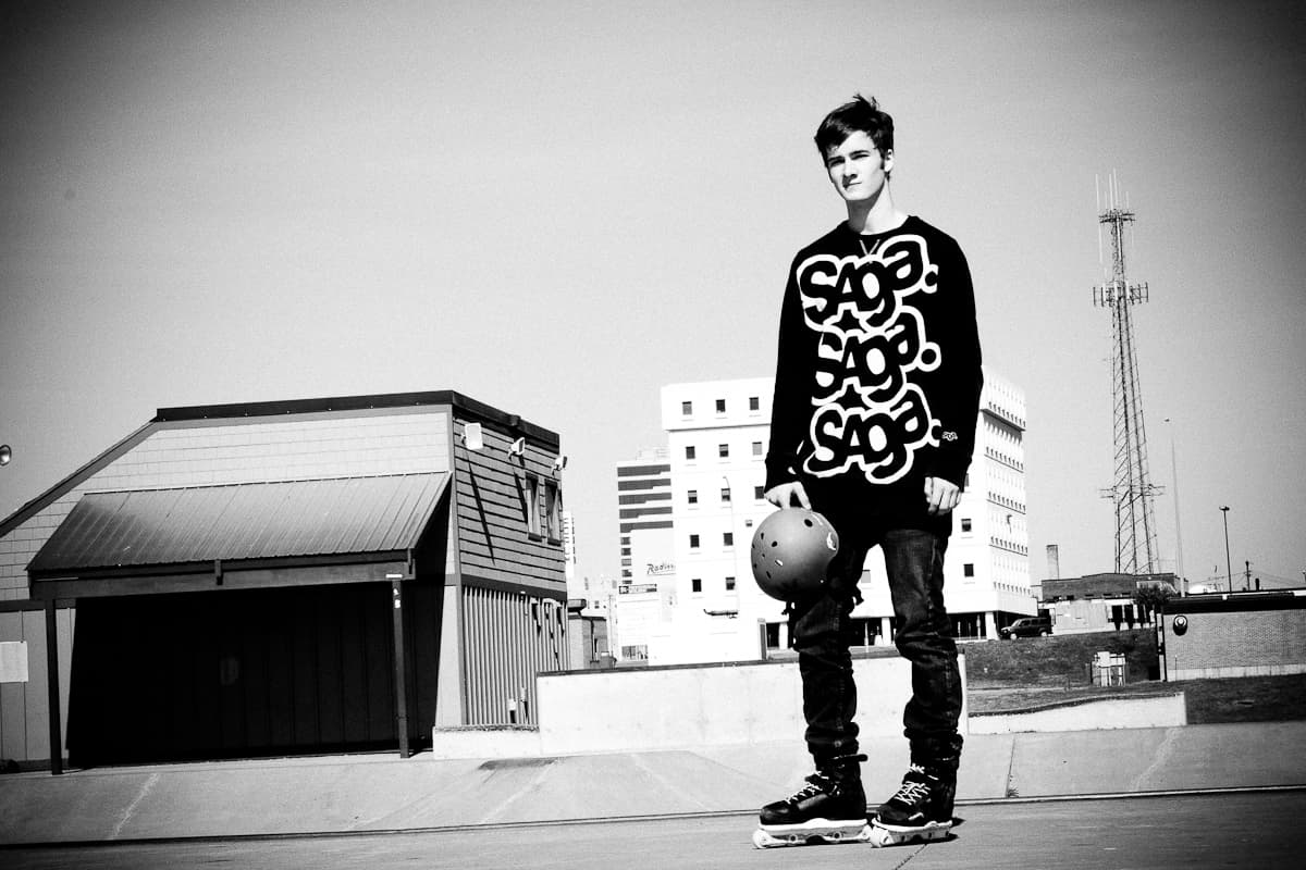 Ryan standing on a parking ramp roof in inline skates holding his helmet, the downtown skyline behind him, in black and white.